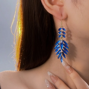 Macro view of blue crystal teardrop leaf drop earrings in gold setting worn on ear