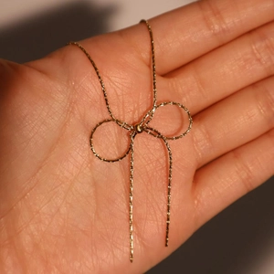 Detail of a delicate golden bow necklace pendant held in hand to show the fine chain craftsmanship