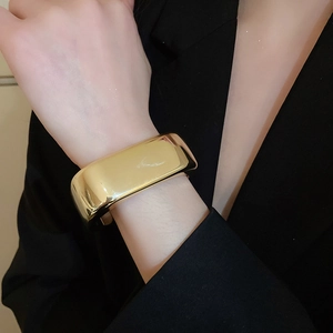 Close-up of polished gold wide wave cuff bracelet worn on model wrist over black suit