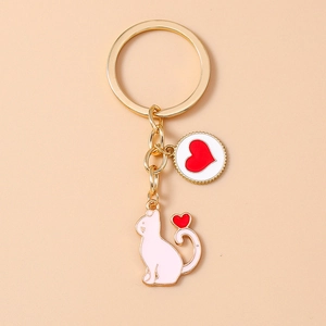 Close-up of golden keychain featuring white enamel cat and round heart pendant