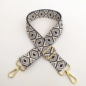 Detailed view of adjustable black and white jacquard bag strap with gold metal lobster clasps