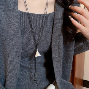 Detail of silver triangle pendant on black cord worn over a grey knit sweater