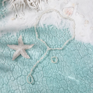 Elegant pearl body chain and matching ring set displayed on white sand with a starfish