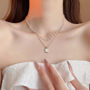 Close-up of double layer gold necklace with square pendant and elegant pearl choker strand