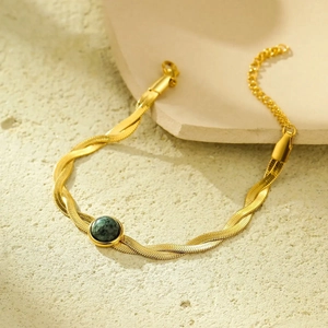 Gold-plated flat snake chain bracelet with a round green gemstone on stone background
