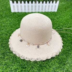 Détail d'un chapeau de paille beige avec perles en coquillage et bordure ondulée sur herbe