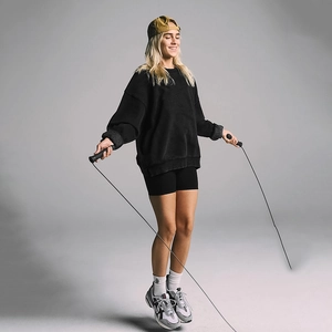 Detail of a woman in a black oversized sporty sweatshirt holding a jump rope in a studio