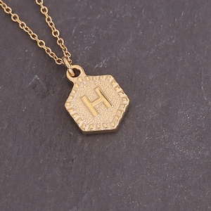 Macro view of a gold hexagonal pendant with a raised initial H and radiating sunburst texture