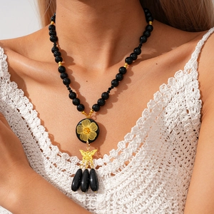 Detail of vintage beaded necklace featuring black beads and golden flower butterfly pendant