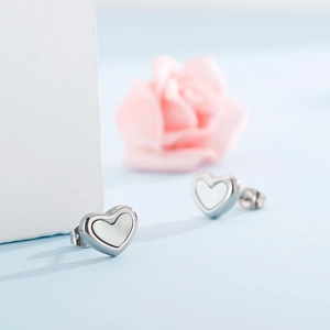 Macro shot of silver heart earrings featuring white shell inlay and a delicate pink rose