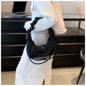 Fashionable black pleated handbag with long fringe straps held by a model in tweed suit