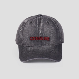 Detailed view of red CONQUER embroidery on a vintage grey washed denim baseball cap