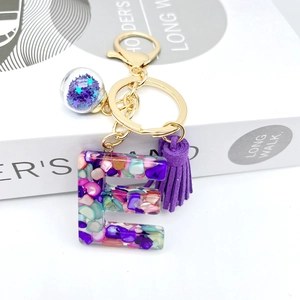 Detail of resin letter E keychain with purple tassel and star sequins glass ball charm