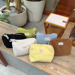 Detailed view of plush lamb wool cosmetic bags in various colors on a wooden bench