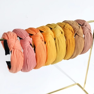 Cross-knotted knitted headbands in assorted warm colors on a gold metal stand