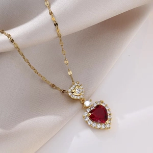 Detailed close-up of 18K gold heart necklace with red gemstone on soft silk fabric