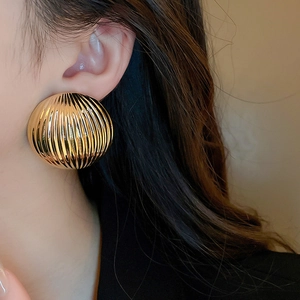 Close-up of golden chunky hoop earrings with ribbed texture on a model's ear