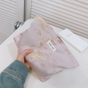 Trousse à maquillage jacquard rose avec broderies dorées tenue par une femme à la main