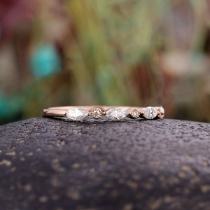 Makroaufnahme: Roségoldener Ring mit Markise- und Rundkristallen auf dunklem Stein