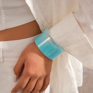 Close-up of a wide sky blue resin bangle with water ripple texture worn by a model