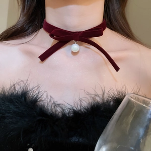 Detail of burgundy velvet bow choker with white pearl pendant on elegant model