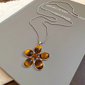 Detail of tiger eye stone flower pendant necklace with silver bead chain on book