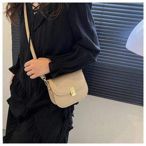 Detail of a beige vintage saddle bag with gold metal buckle on a model in a black skirt
