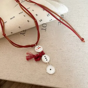 Detail of a snowman charm necklace with festive red tassels and woven cord