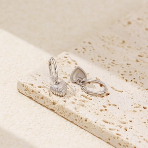 Macro shot of silver heart earrings with shell texture on beige stone display