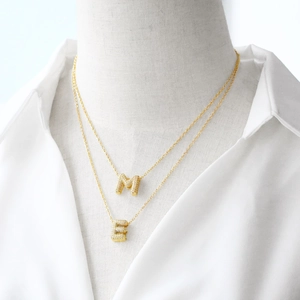 Layered gold necklace featuring zircon-encrusted M and E alphabet pendants on a model