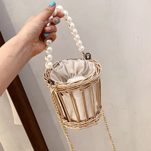 Straw woven bucket bag with pearl handle and metal chain in cream and natural wood tones
