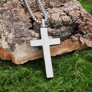 Vintage two-tone stainless steel cross pendant on a bead chain over natural moss background