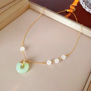Golden ginkgo leaf necklace with green donut pendant and white beads on a display box