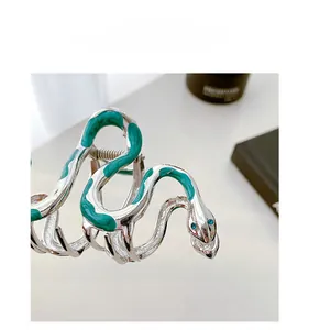 Macro shot of silver snake hair claw with green enamel detail and blue crystal eyes
