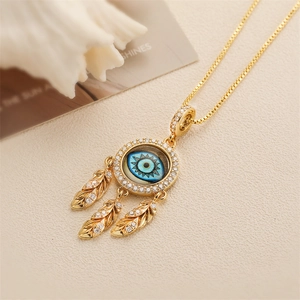 Collana occhio del male dorata con zircone blu e tre ciondoli a piuma su sfondo beige