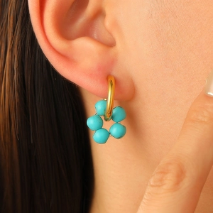 Close-up of model wearing a gold hoop earring with a blue beaded flower pendant