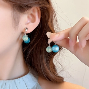Dettaglio di orecchini con perline verdi e blu indossati su modella per uno stile estivo