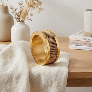 Close-up of wide gold stainless steel ring with woven chain texture on linen background