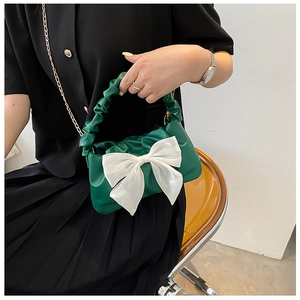 Detail of green pleated handbag with a large white bow and elegant gold chain strap