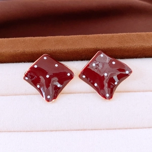 Close-up of square burgundy polka dot stud earrings on a velvet jewelry display box