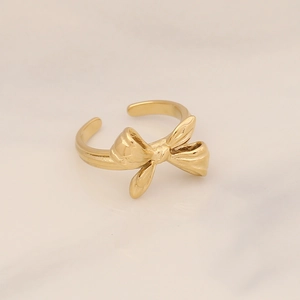 Detailed view of adjustable golden bow ring with polished metallic finish on marble background
