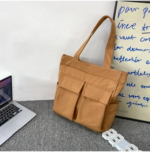 Detail of canvas tote bag with dual front utility pockets on a minimalist grey rug