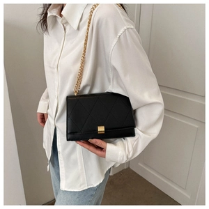 Detail of black quilted shoulder bag featuring gold chain strap and metal lock closure