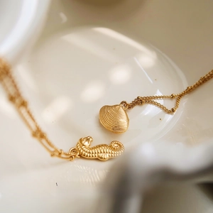 Close-up of golden seahorse and seashell pendants on beaded chain on white ceramic dish
