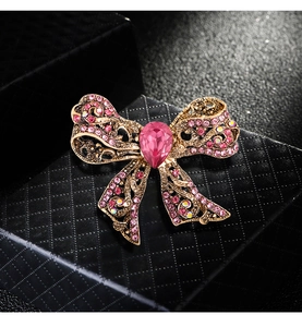 Macro shot of gold bow brooch featuring pink rhinestones and a central teardrop gemstone