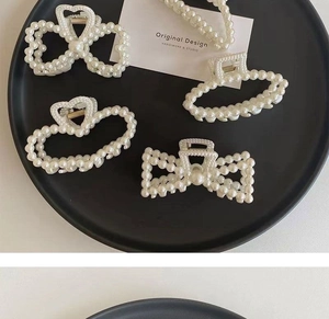 Detailed view of four pearl hair claws in bow, heart, and rectangle shapes on a tray