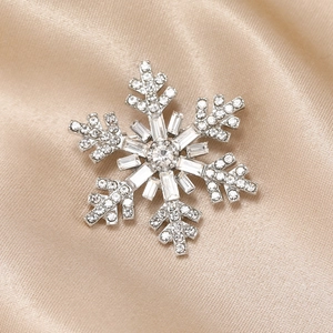 Elegant silver snowflake brooch with sparkling rhinestones on champagne silk fabric
