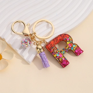Detail of resin letter R keychain with colorful sequins, gold hardware and purple tassel