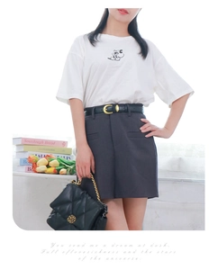 Close-up of a stylish black leather belt with a golden C-shaped buckle on a grey skirt