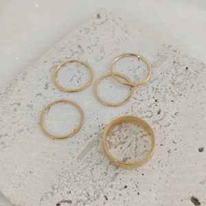 Stackable set of five minimalist gold stainless steel rings on a white stone tile